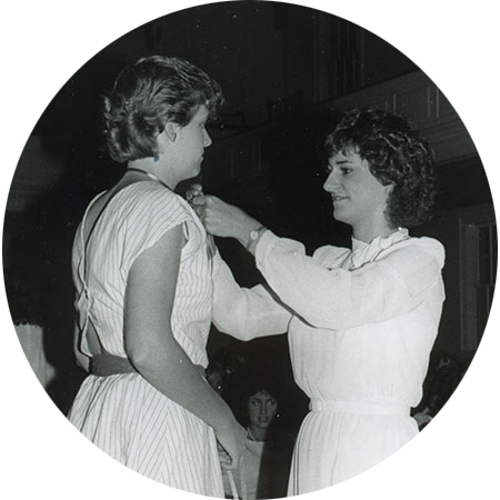 Woman pinning a ribbon on the collar of another woman.