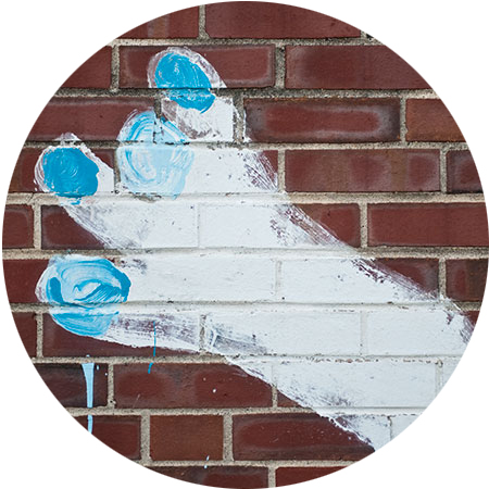 Painting of a foot with blue toenails on a brick wall. 